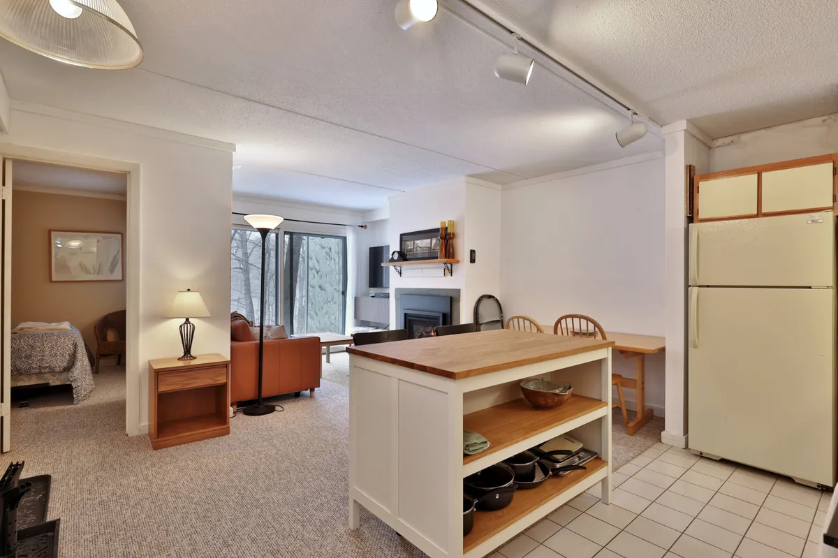 This image offers a wide perspective of the living space, featuring a kitchen island, fireplace, sliding glass doors, and a comfortable seating area. Natural light pours in through the glass doors, connecting the interior to landscaped grounds outside, and providing a bright, airy feel ideal for both relaxing and socializing.