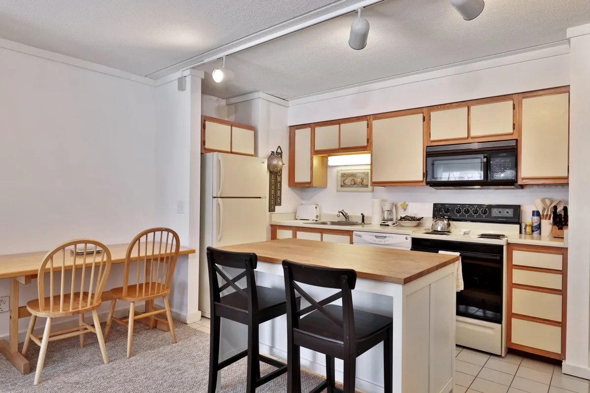 A cozy and inviting interior kitchen scene, featuring a kitchen island, dining table, and modern appliances. The setup hints at a warm, comfortable place to gather and prepare meals after a day on the slopes.
