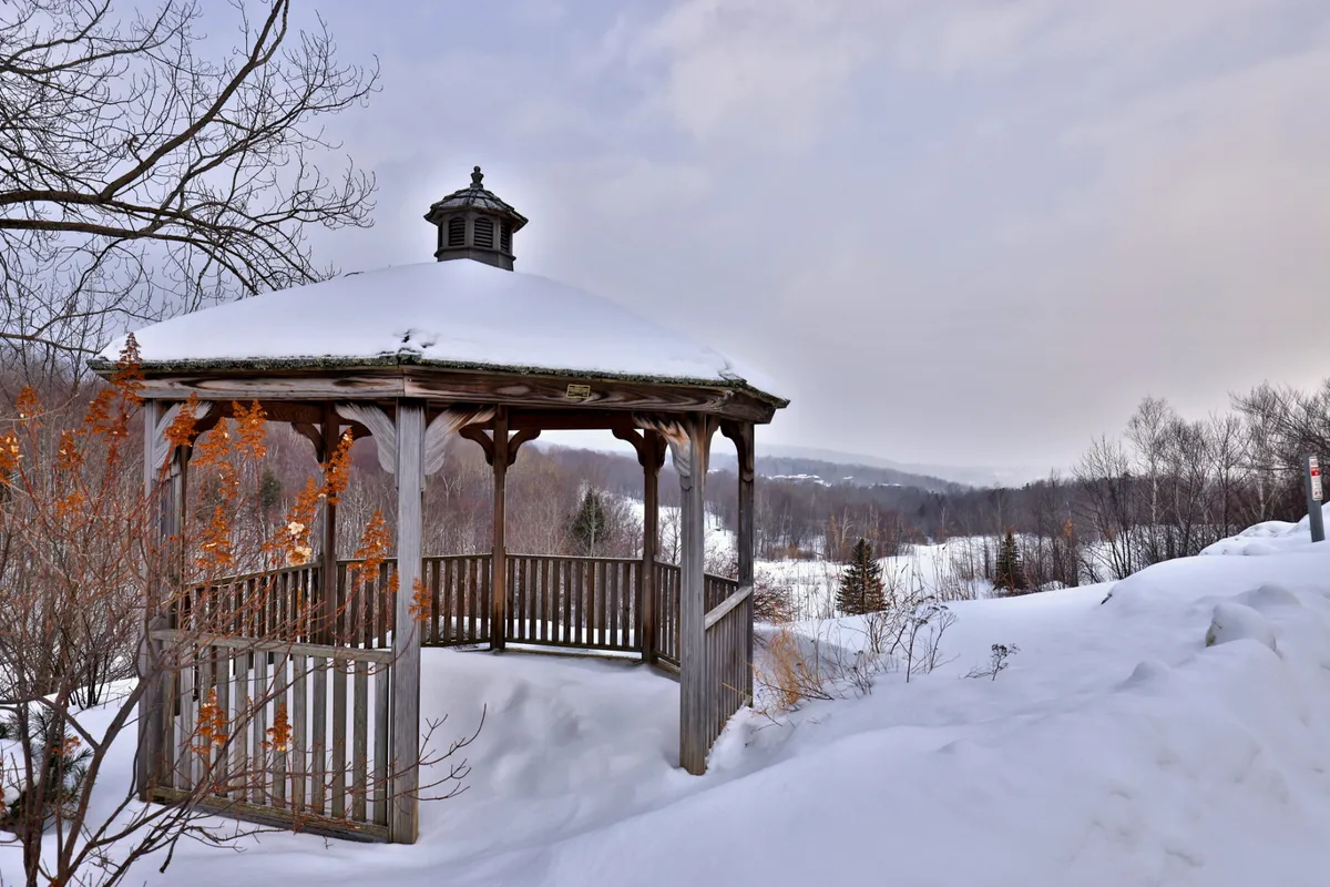 A wooden gazebo surrounded by a snowy landscape and bare trees, creating a peaceful, atmospheric spot perfect for unwinding after an evening out.