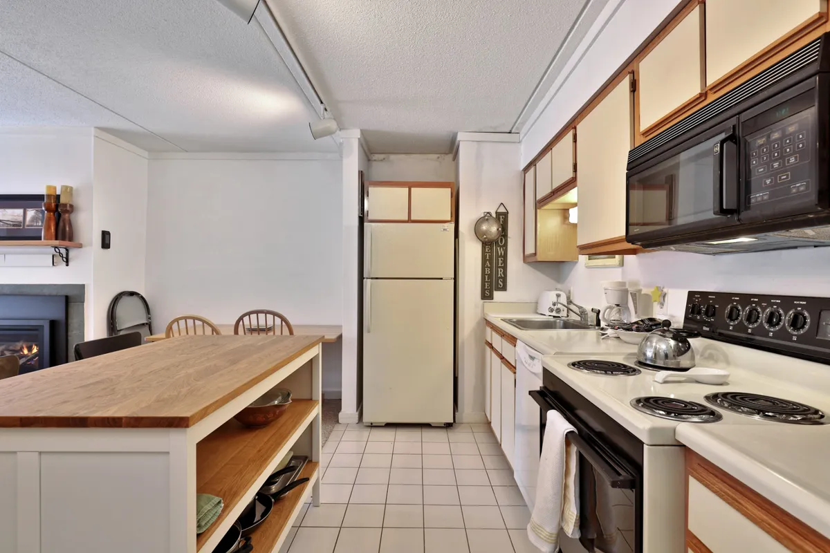A cozy kitchen with a central island, stove, and full-size refrigerator, presenting a practical and inviting cooking space. The setup allows for easy meal preparation and casual dining, with ample counter space for group cooking.