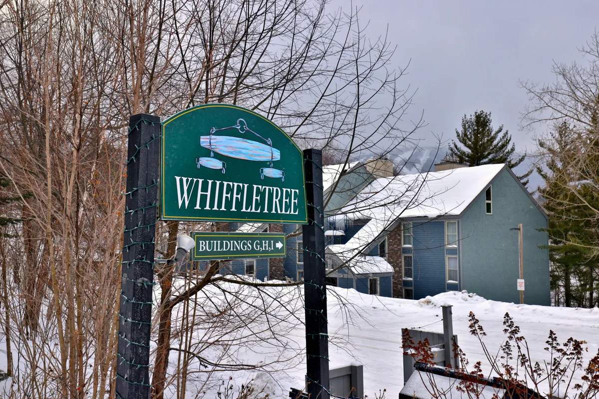 A warmly lit Whiffletree sign stands out amid freshly fallen snow, with snowy buildings in the background indicating a welcoming winter resort vibe. The surrounding area is covered in pristine snow, setting the scene for classic ski lodge experiences and easy access to winter activities.