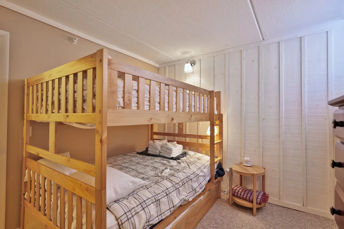 This image highlights a bunk bed setup in a well-lit room, complete with a nightstand and decorative wall accents. The arrangement is inviting, perfect for sleepovers or accommodating multiple guests, and reflects a playful yet cozy atmosphere.