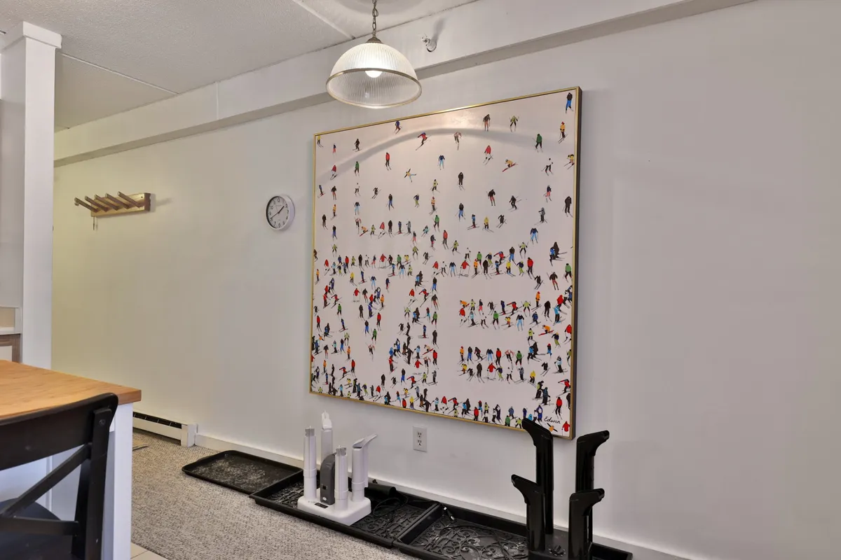 A vibrant interior space featuring a large colorful artwork, hanging light fixture, clock, and coat rack—suggesting a lively, community-oriented common area ideal for socializing or relaxing indoors.